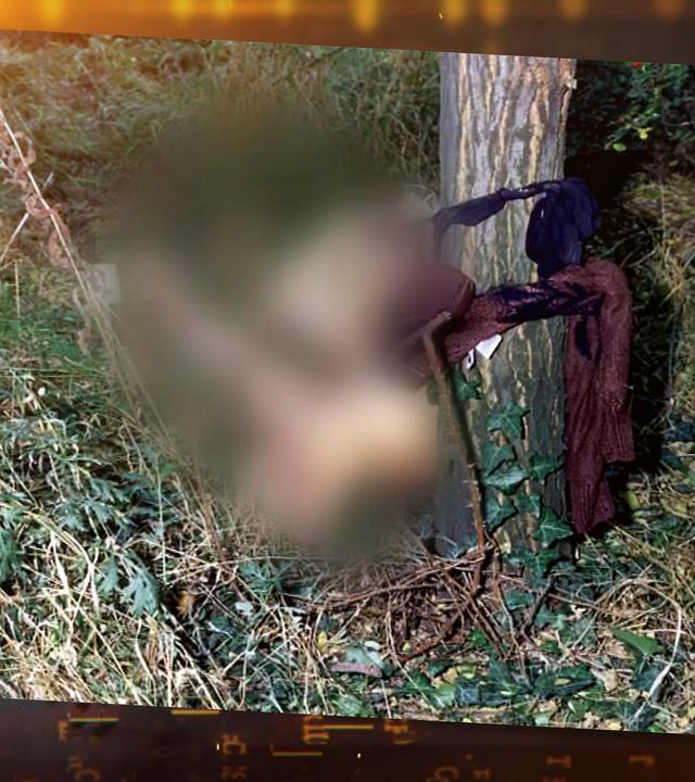 Tatort-Foto: Die unbekleidete Leiche einer jungen Frau in sitzender Position auf einer Wiese, ihre nackter Oberkörper ist mit einem blauen BH und einem braunen Pullover an einen Baum gebunden.