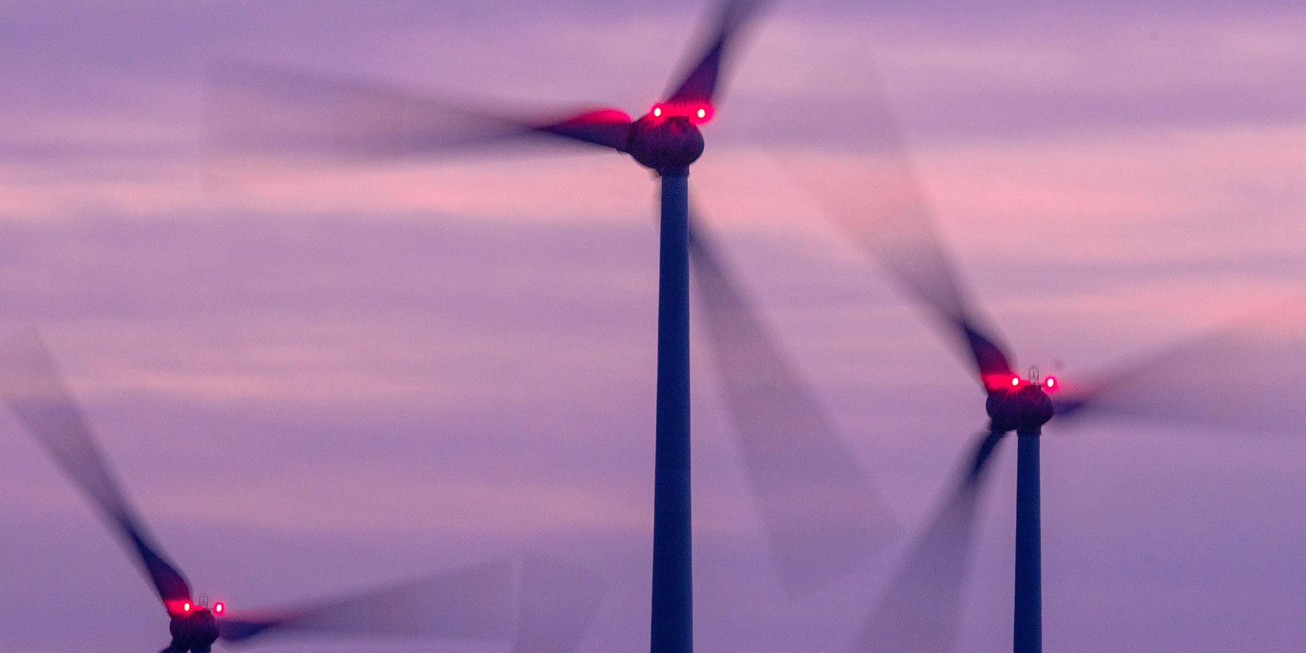 Mit Signallampen beleuchtete Windräder drehen sich nach Sonnenuntergang in einem Windpark. 