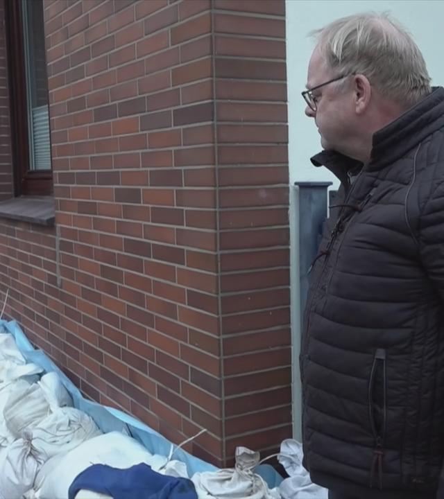 Auf dem Bild ist ein Mann zu sehen, der gerade sein Haus mit den Säcken davor anschaut.