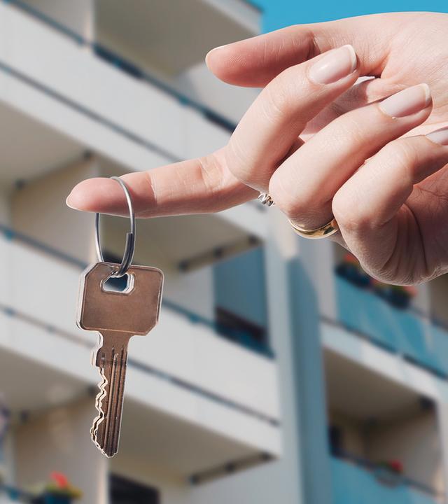 Wohnungsschlüssel in der Hand vor einem Mehrfamilienhaus