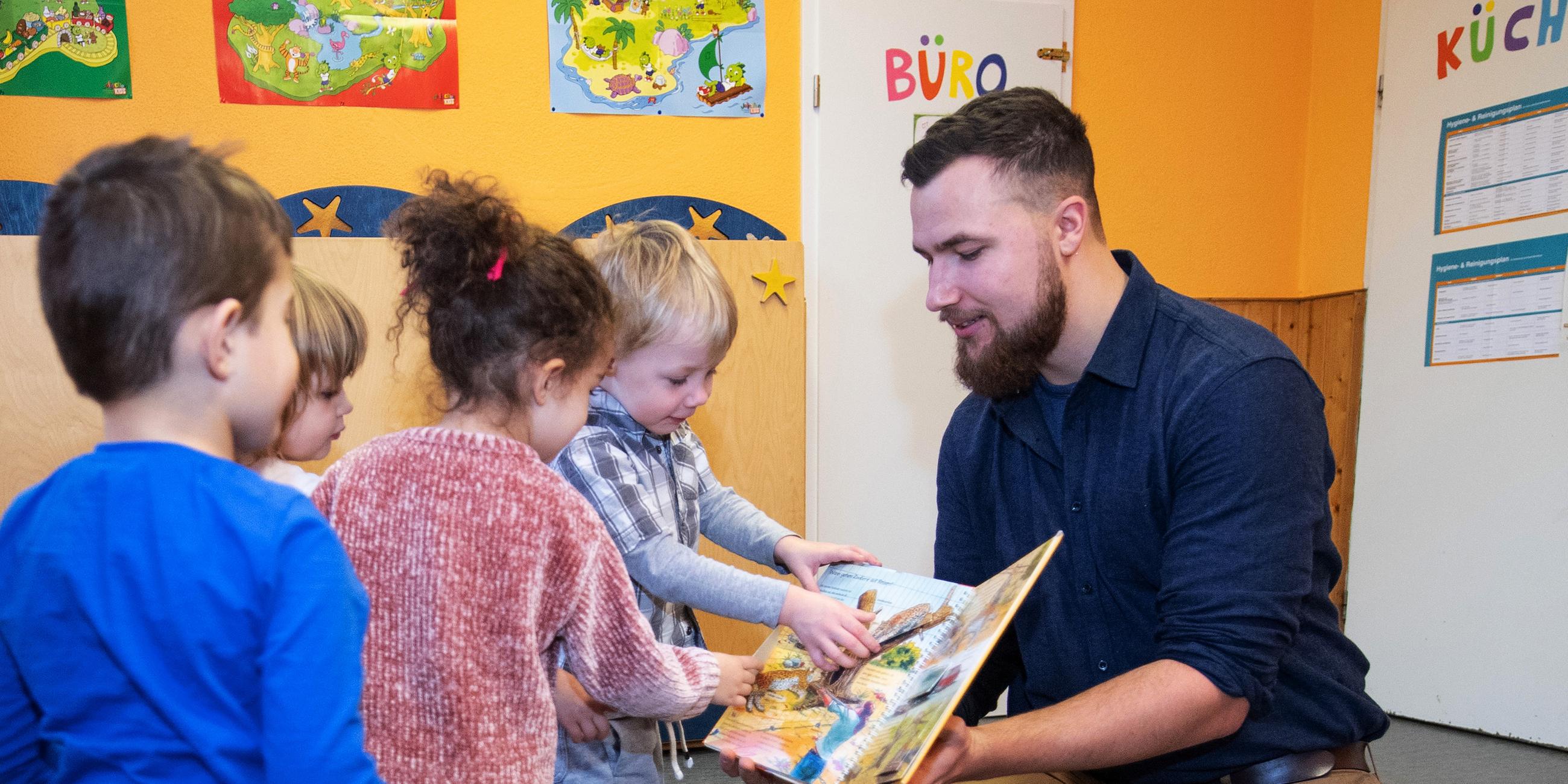 Ein Erzieher zeigt Kindern im Kindergarten ein Buch, aufgenommen am 0.01.2019