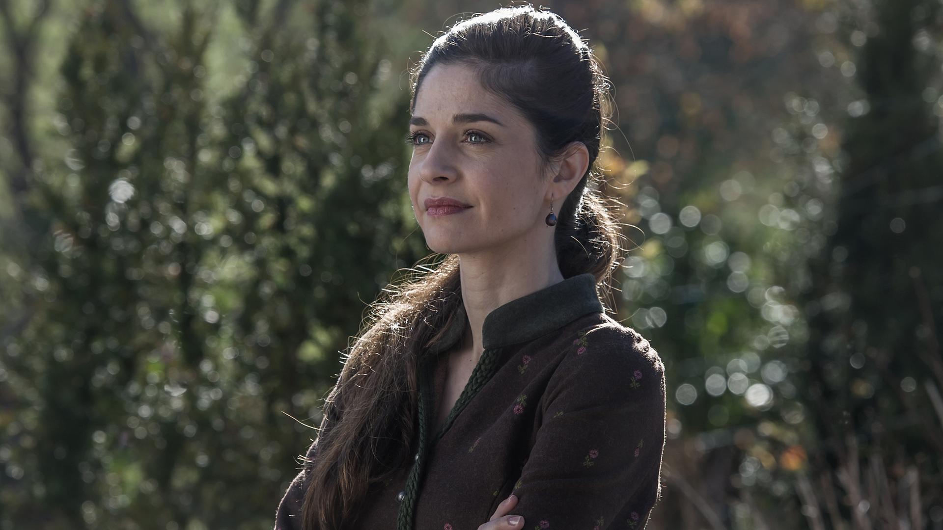 "Der Bergdoktor - Erzwungene Liebe": Kara Lambert (Anne Werner) steht im Grünen und blickt in die Ferne.