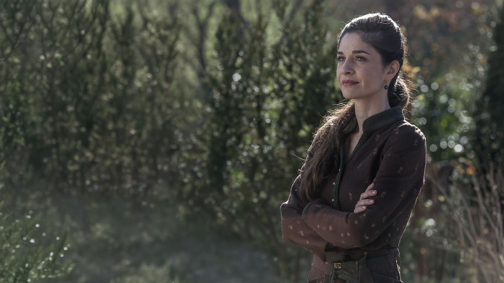 "Der Bergdoktor - Erzwungene Liebe": Kara Lambert (Anne Werner) steht im Grünen und blickt in die Ferne.