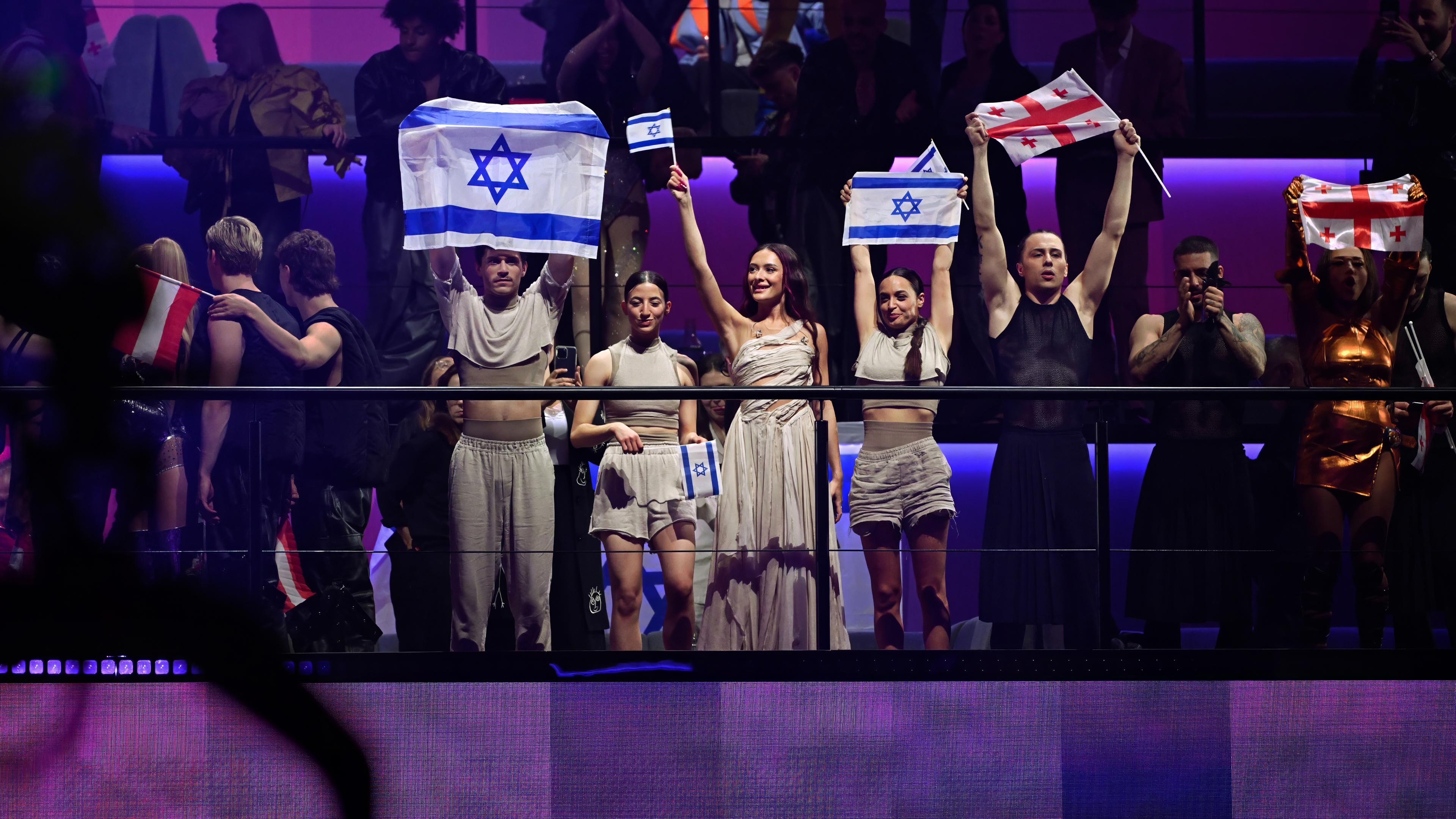Auf einer Tribühne stehen mehrere junge Menschen in Kostümen und halten israelische Flaggen hoch.