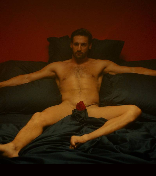 "Escort Boys - Ein letztes Mal": Ben (Guillaume Labbé) liegt nackt auf einem schwarzen Bett in einem Schlafzimmer. Eine Rose bedeckt seinen Schoß. Das Licht ist gedimmt, auf dem Nachttisch brennen Kerzen und tauchen den Raum in warmes Licht.
