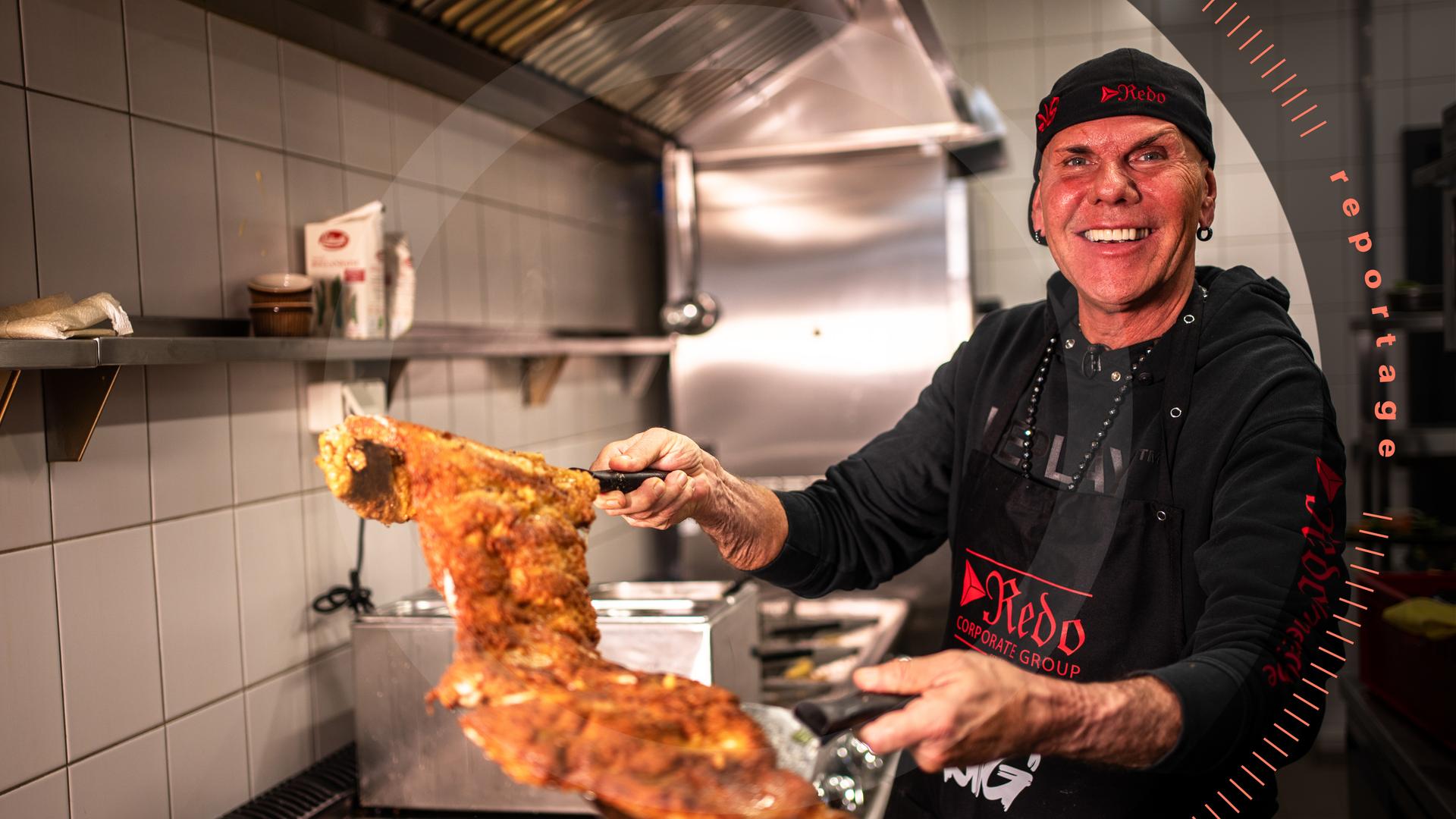 Koch René Dost posiert in seiner Küche mit einem großen panierten Schnitzel.