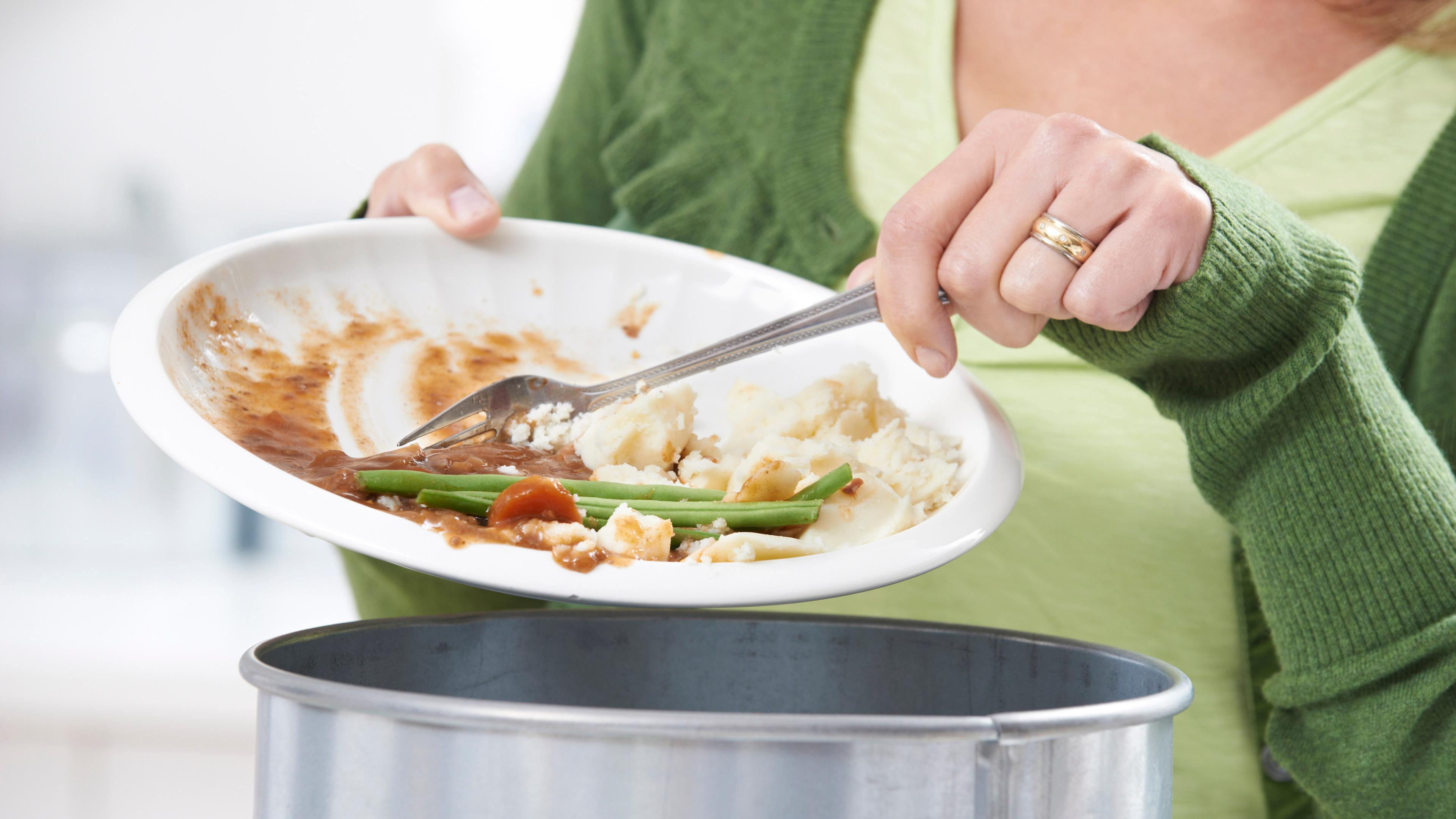Eine Frau schiebt mit einer Gabel Essensreste von einem Teller in einen Topf.