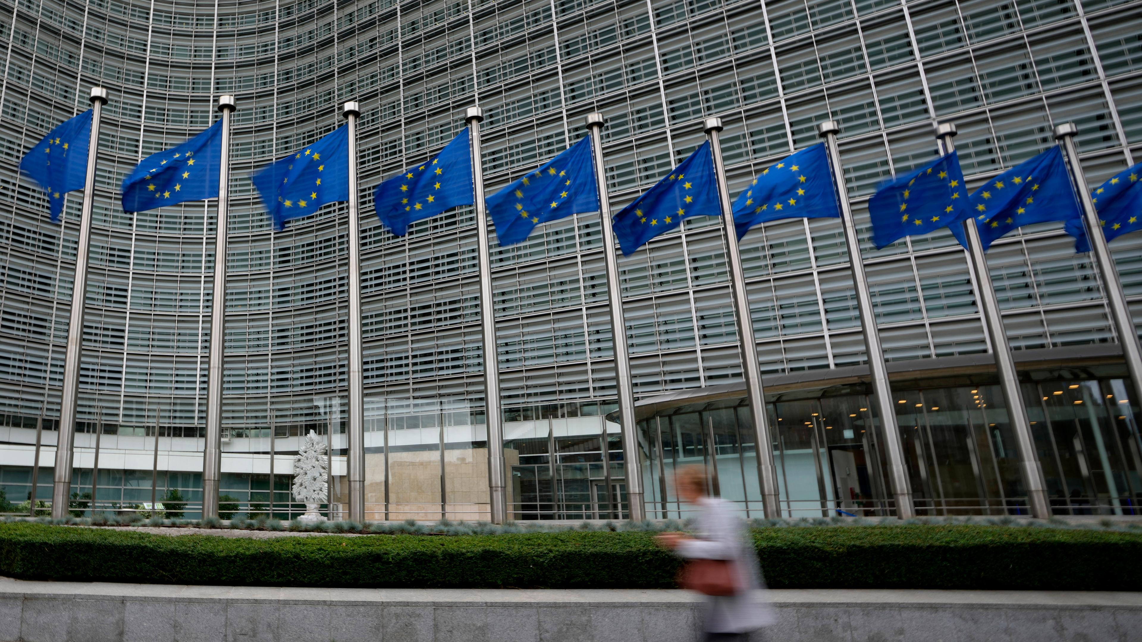 Belgien, Brüssel: EU-Fahnen flattern im Wind, während eine Person am Hauptsitz der EU vorbeigeht