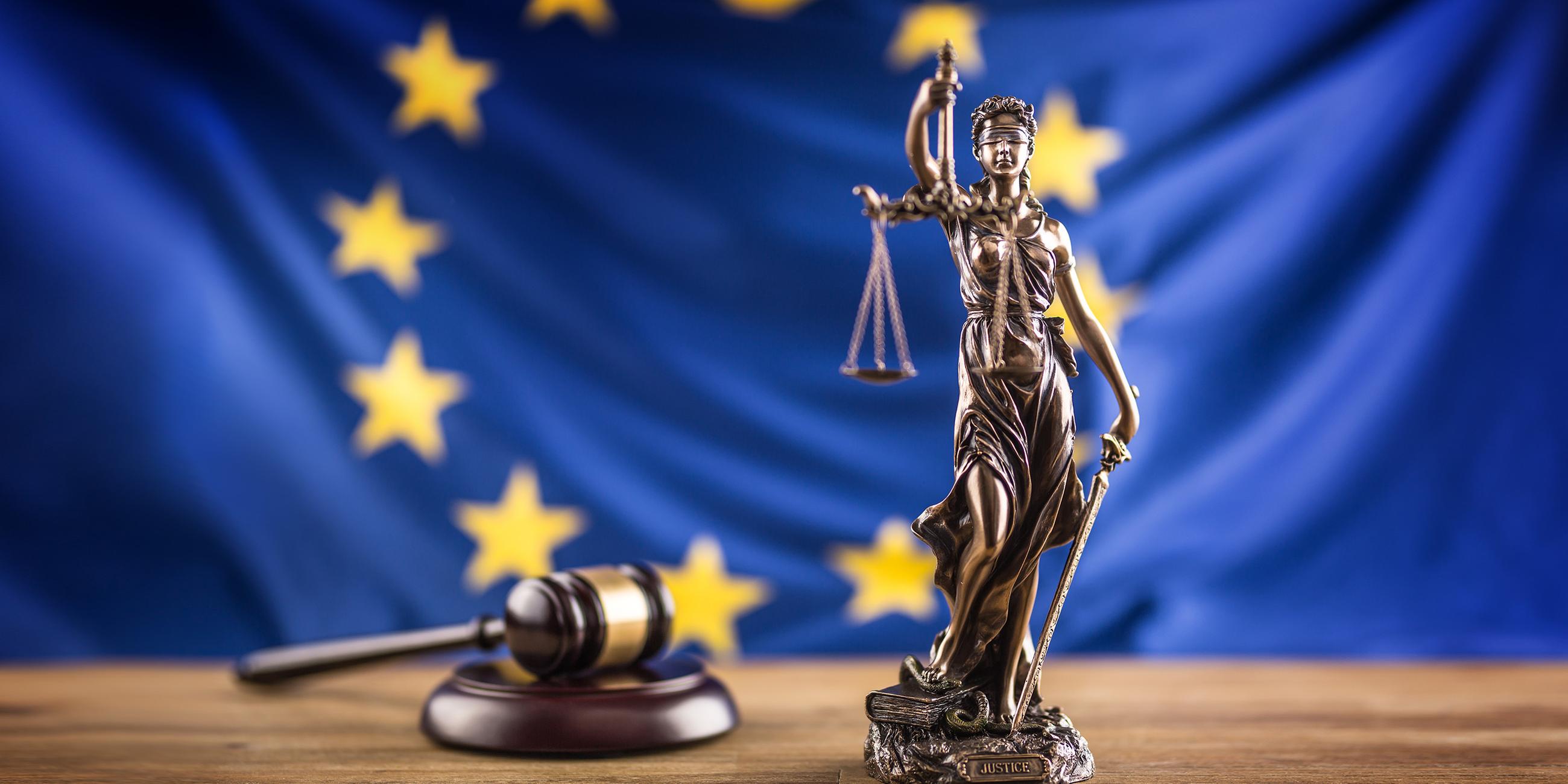 Richterhammer und Figur der Justitia vor Europa-Flagge
