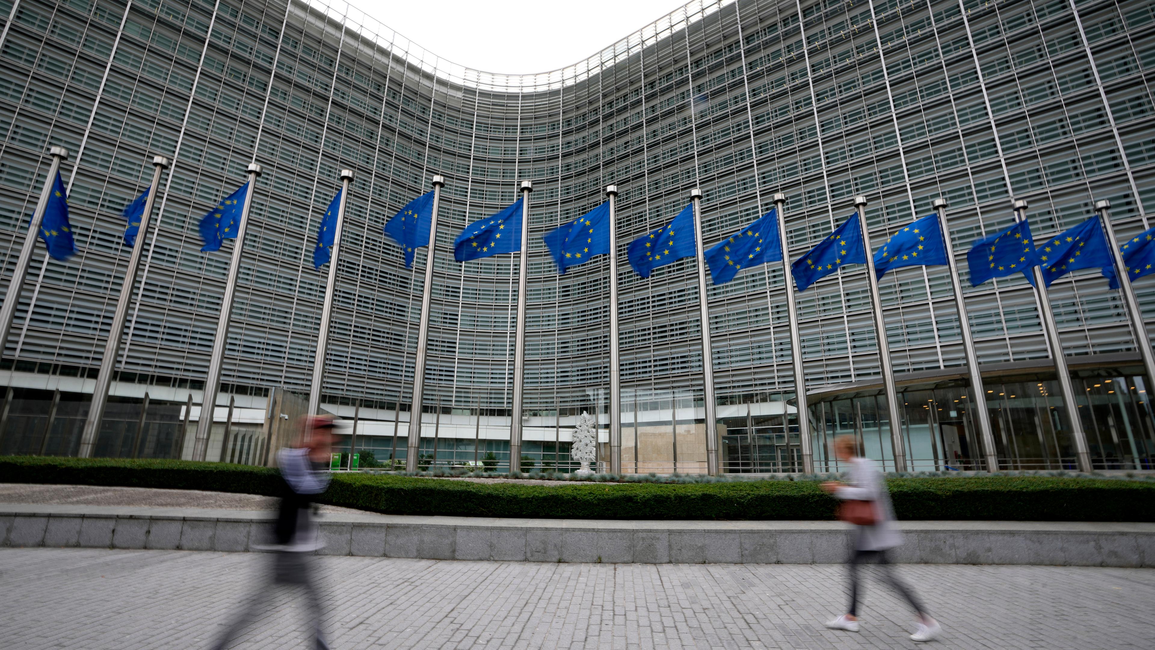 Die Flaggen der Europäischen Union wehen im Wind, während Fußgänger an der Zentrale der EU-Kommission vorbeigehen.