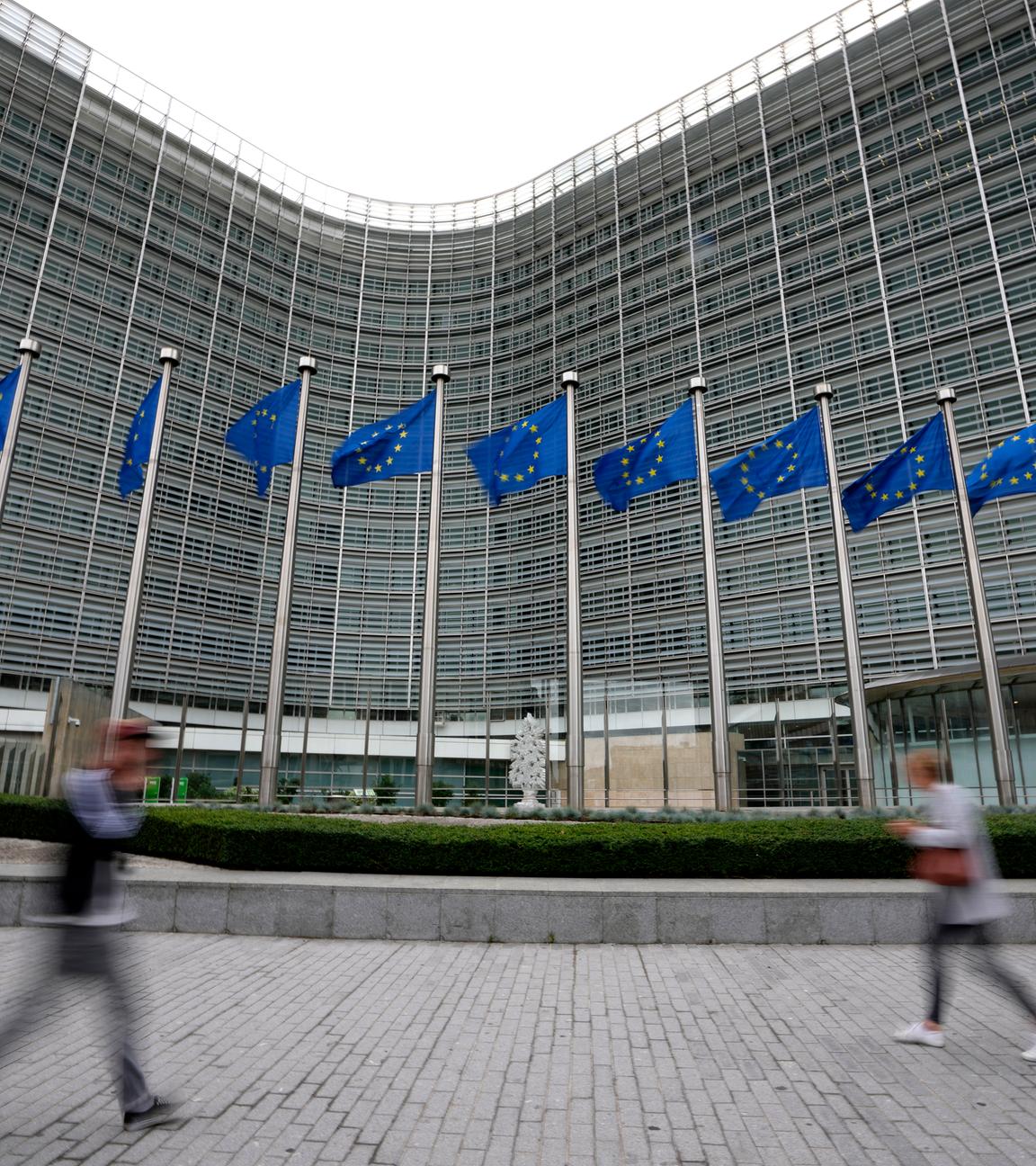 EU-Fahnen flattern im Wind, während Fußgänger am EU-Hauptsitz vorbeigehen. 