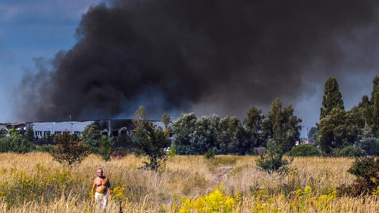 Menschen gehen über ein Feld, während an der Einschlagstelle eines russischen Angriffs nahe Kiew (Ukraine) am 31. August 2026 Rauch aufsteigt – inmitten der russischen Invasion.