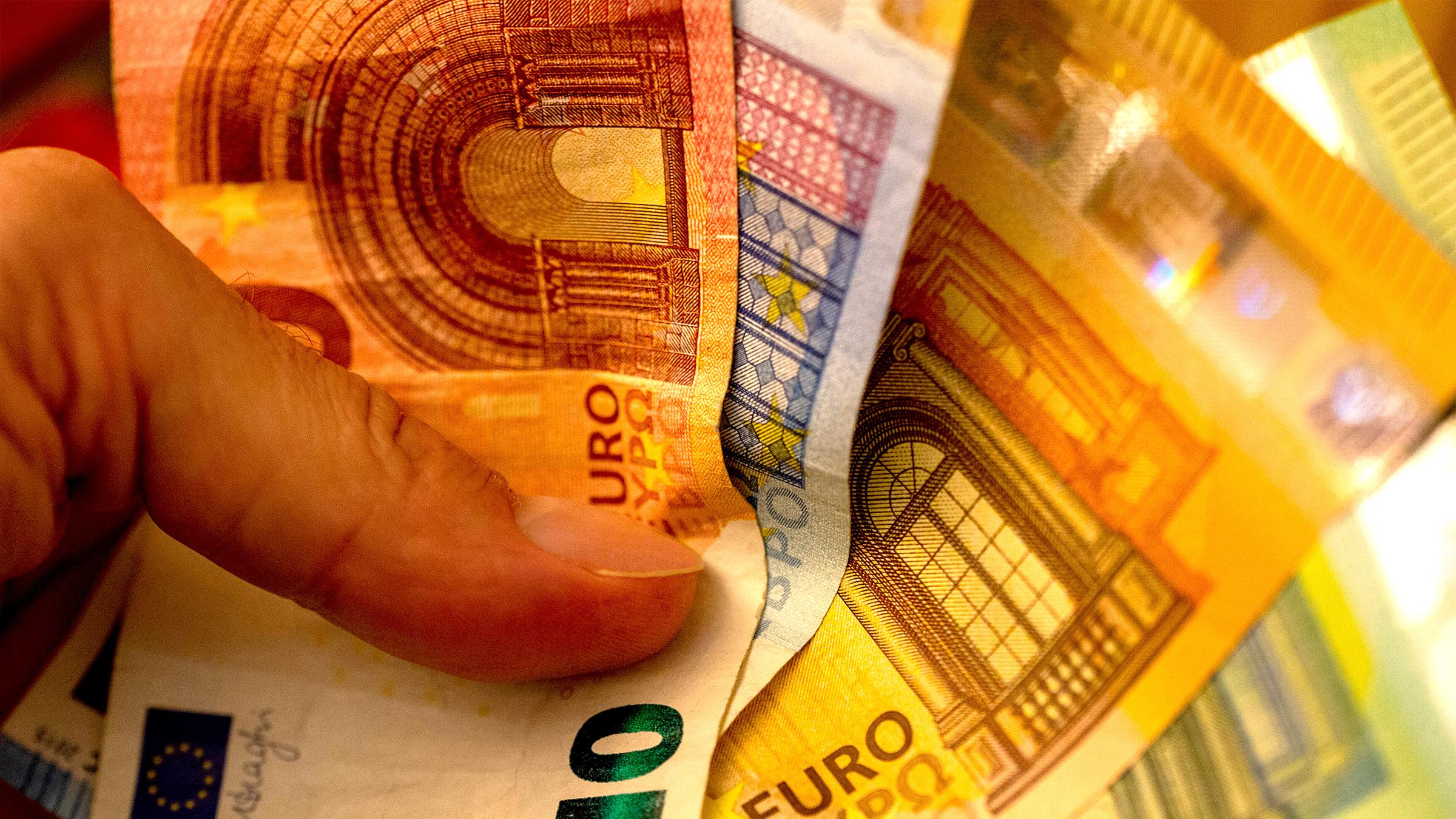 Ein Mann hält einen Bündel mit Eurobanknoten zur Bezahlung in der Hand