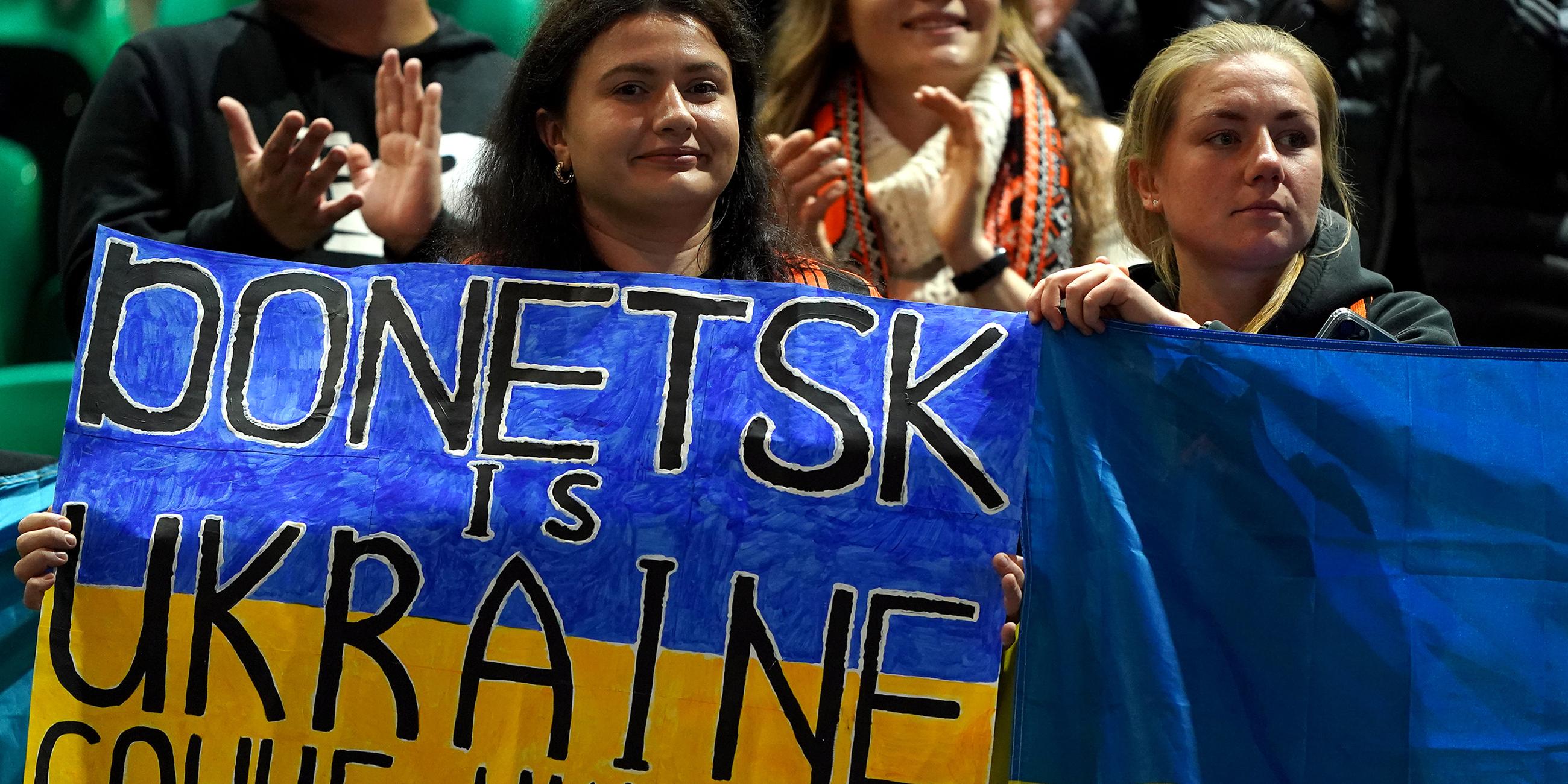 Weibliche Fans von Schachtjor Donezk halten ein Schild mit der Aufschrift "Donezk ist Ukraine" und eine ukrainische Flagge während des Spiels. 