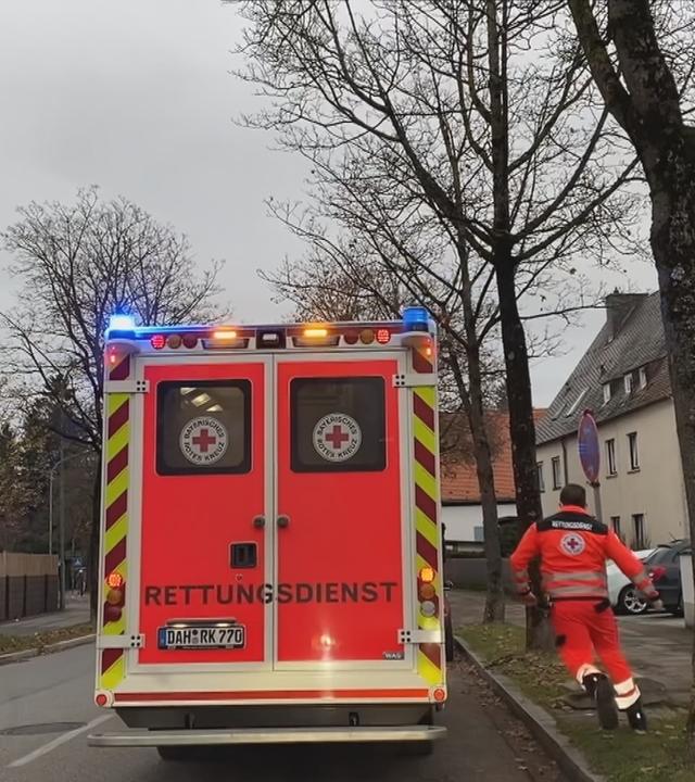 Eine Rettungskraft rennt zu einem Rettungswagen. Das Blaulicht ist an.