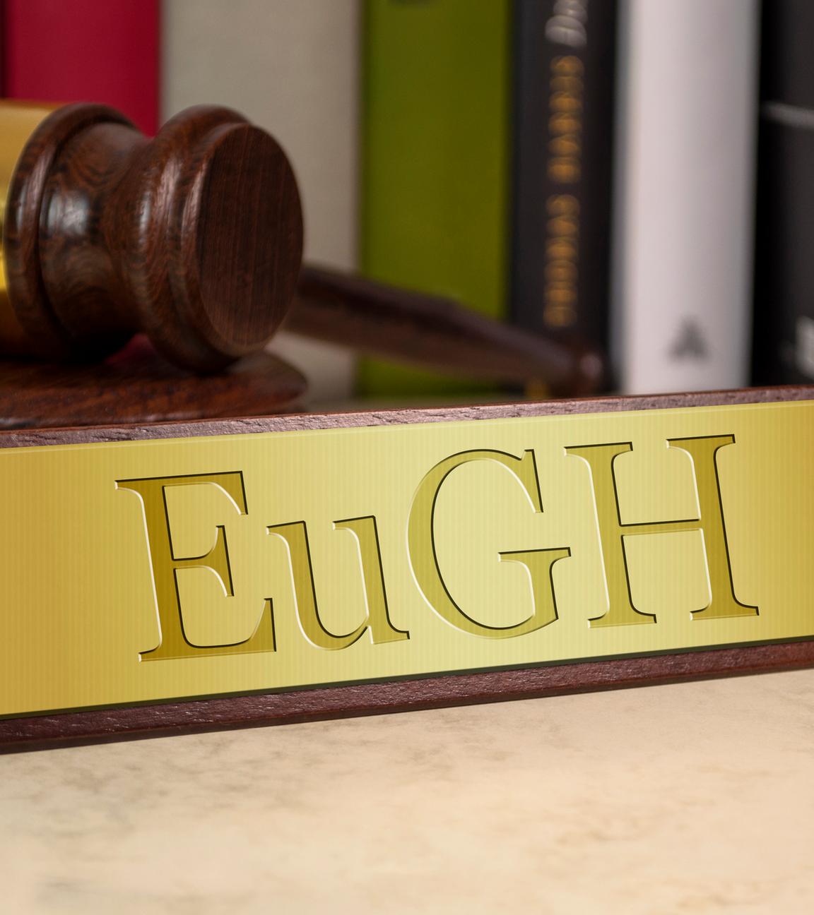 Ein goldenes Schild mit der Aufschrift EuGH steht auf einem Mamor-Tisch. Im Hintergrund sieht man einen Richter-Hammer und einige Bücher.