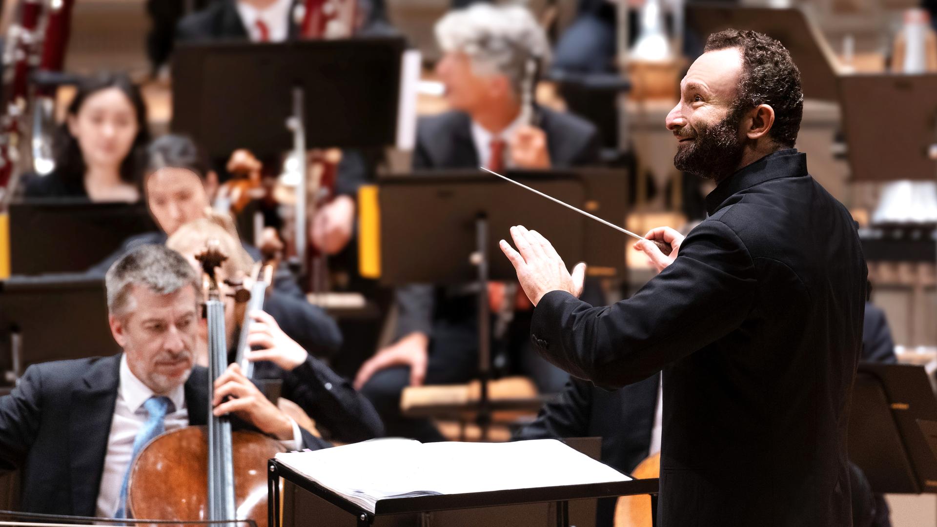 Europakonzert 2026 aus Schloss Esterházy: Musiker der Berliner Philharmoniker sitzen auf einer Bühne. Sie spielen auf ihren Instrumenten. Vor ihnen steht der Dirigent Kirill Petrenko und blickt zur Seite.