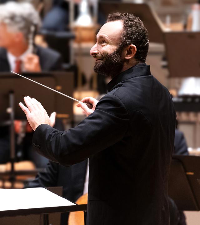 Europakonzert 2026 aus Schloss Esterházy: Musiker der Berliner Philharmoniker sitzen auf einer Bühne. Sie spielen auf ihren Instrumenten. Vor ihnen steht der Dirigent Kirill Petrenko und blickt zur Seite.