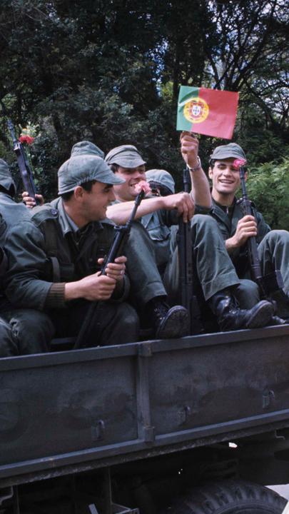 Auf einem Lastwagen sitzen Soldaten mit Nelken in den Gewehrläufen.