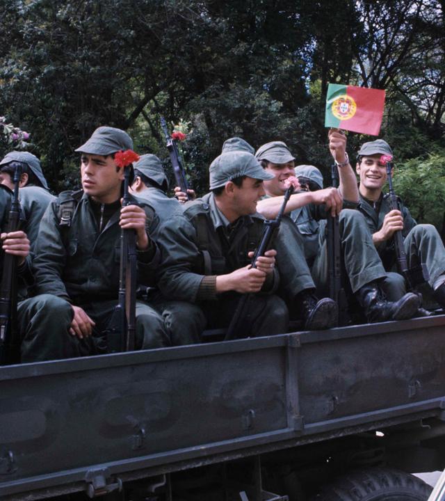 Auf einem Lastwagen sitzen Soldaten mit Nelken in den Gewehrläufen.