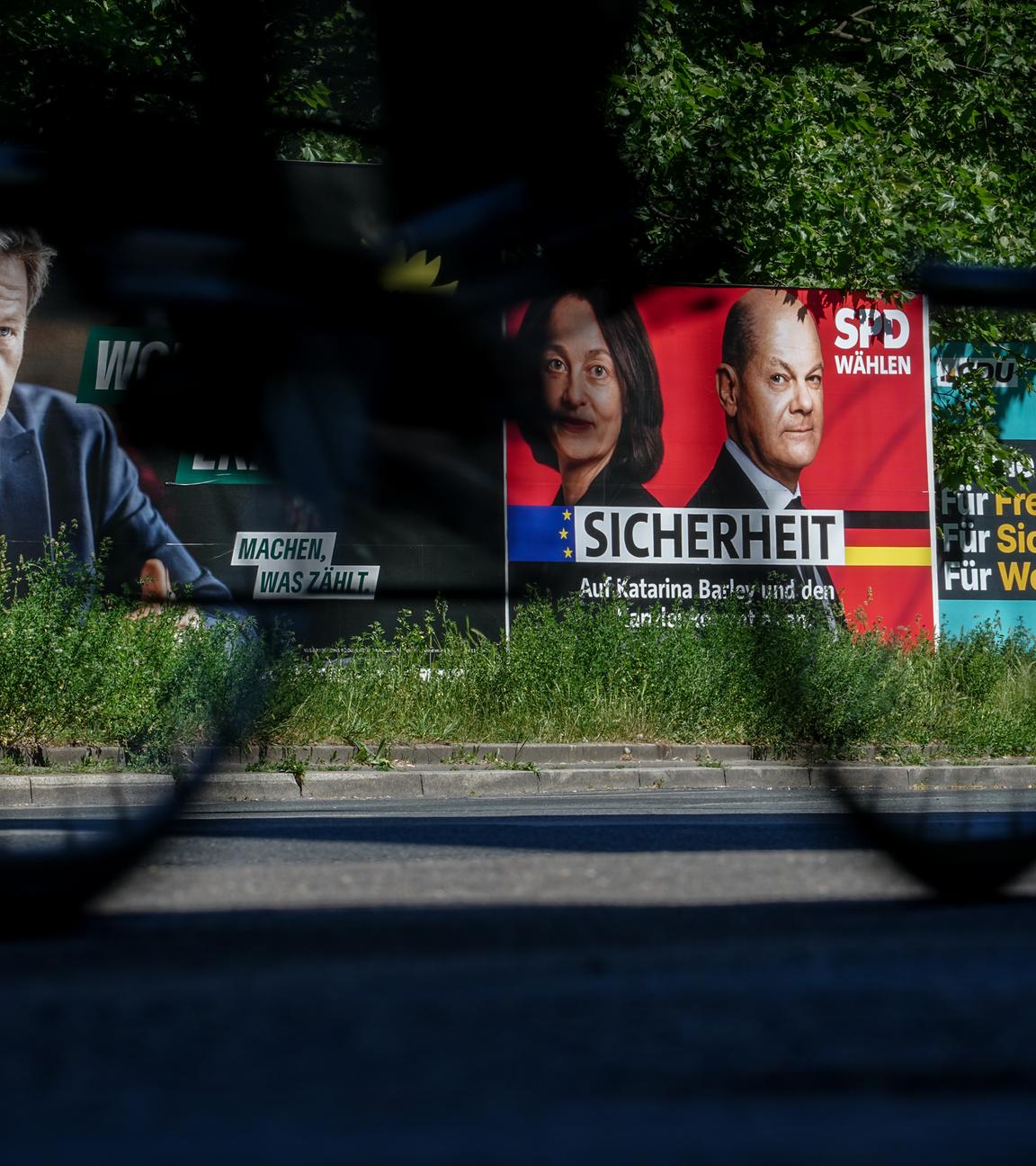 Europawahl - Wahlplakate von den Grünen, der SPD und der CDU stehen auf grünem Rasen. Ein Fahrrad fährt vorbei.