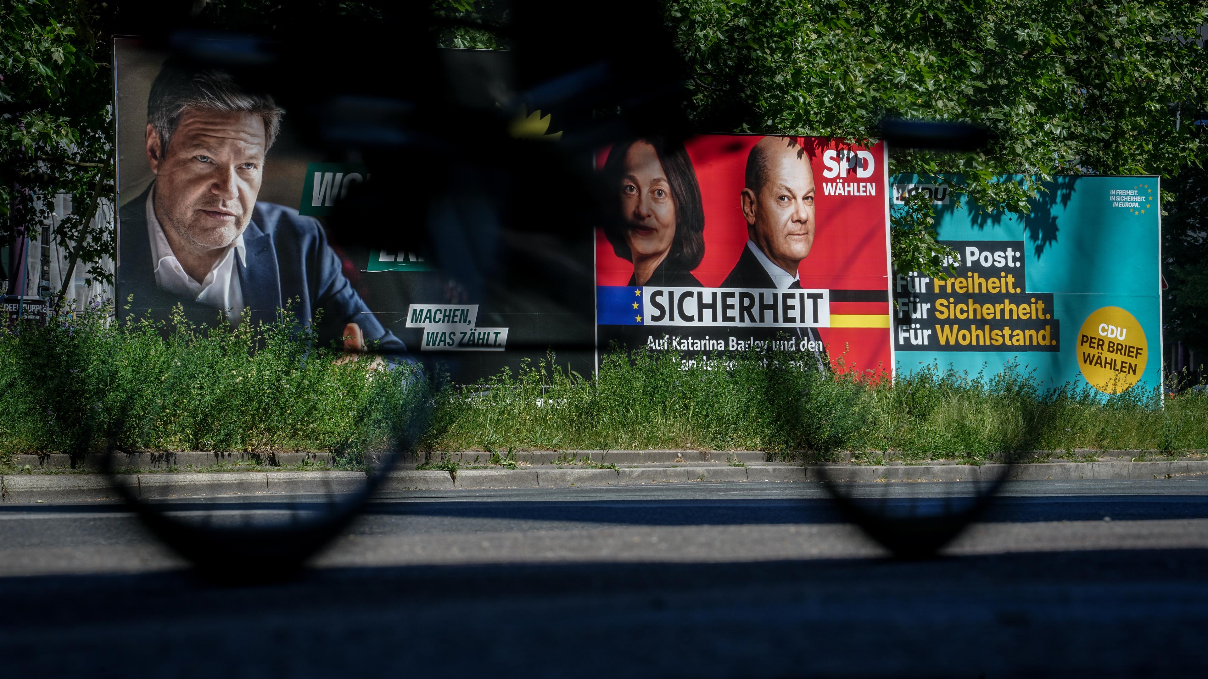 Europawahl - Wahlplakate von den Grünen, der SPD und der CDU stehen auf grünem Rasen. Ein Fahrrad fährt vorbei.