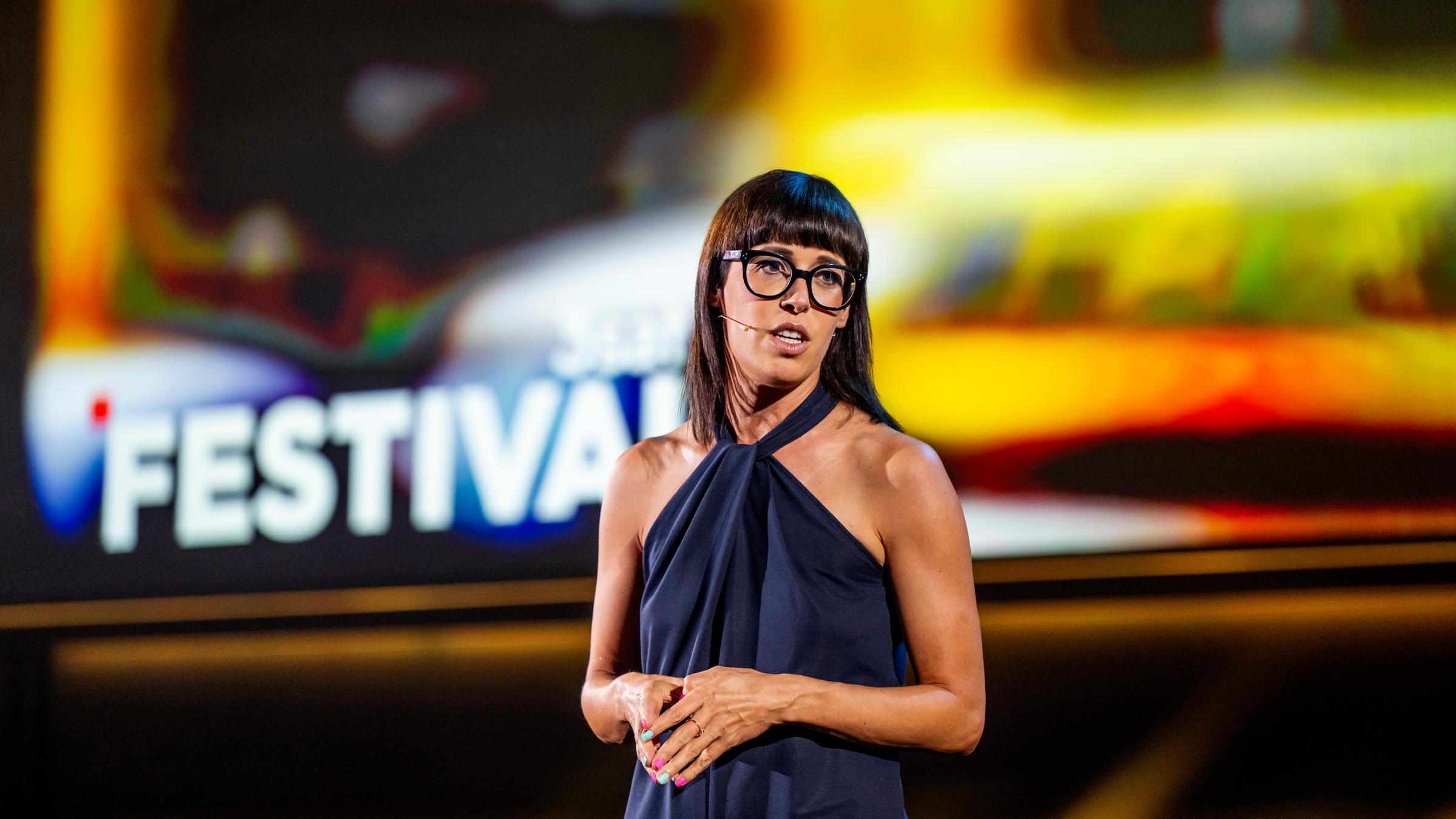 Eva Karl Faltermeier steht in der Mitte des Bildes. Sie faltet die Hände vor ihrem Bauch. Die Bühne im Hintergrund ist gelb beleuchtet. 