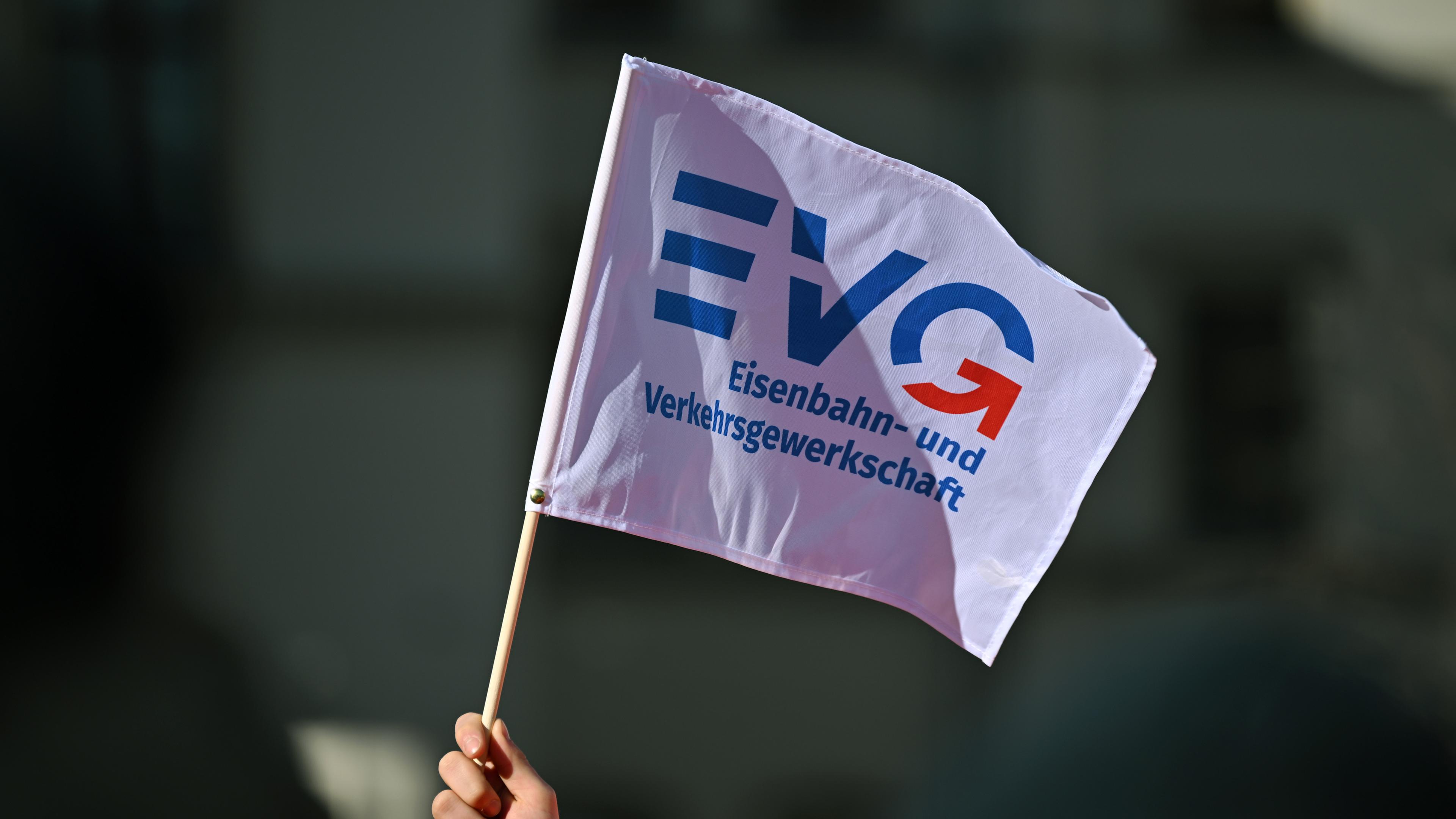 Thüringen, Erfurt: Ein Teilnehmer am Warnstreik vor dem Erfurter Hauptbahnhof schwenkt ein Fähnchen der Eisenbahn- und Verkehrsgewerkschaft EVG.
