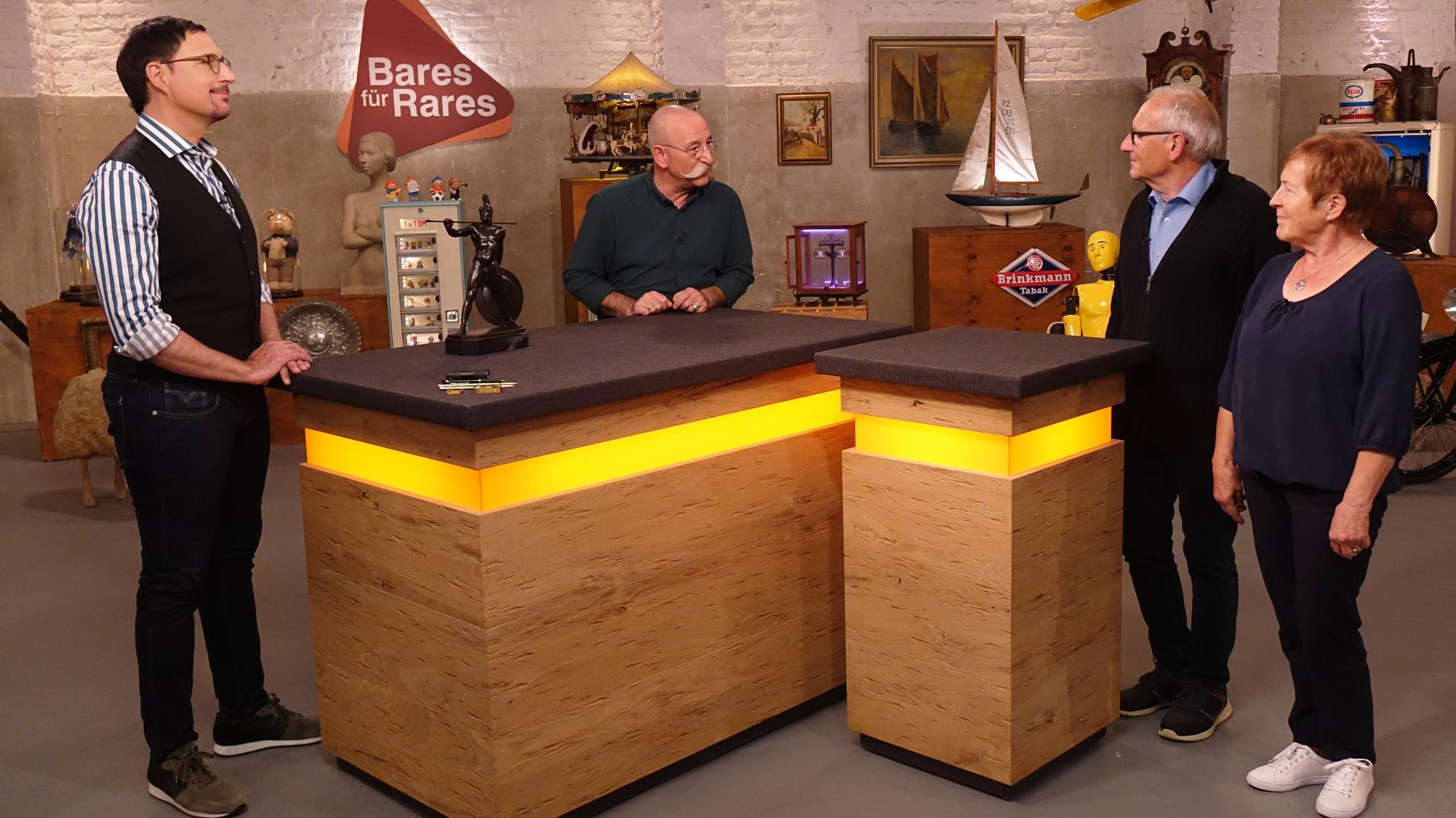 Experte Colmar Schulte-Goltz (links) hat eine Bronzefigur eines Speerwerfers vor sich auf dem Tisch stehen. Er und Horst Lichter (Mitte) schauen das Verkäuferpaar (rechts) an.