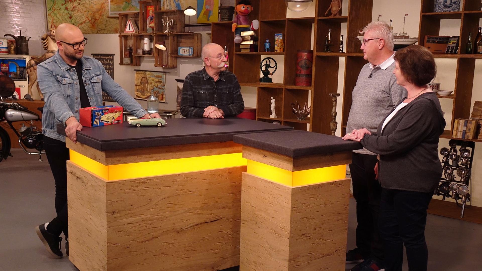 Experte Sven Deutschmanek (links) hat ein Fernlenkauto vor sich auf dem Tisch stehen. Er und Horst Lichter (Mitte) schauen das Verkäuferpaar (rechts) an.