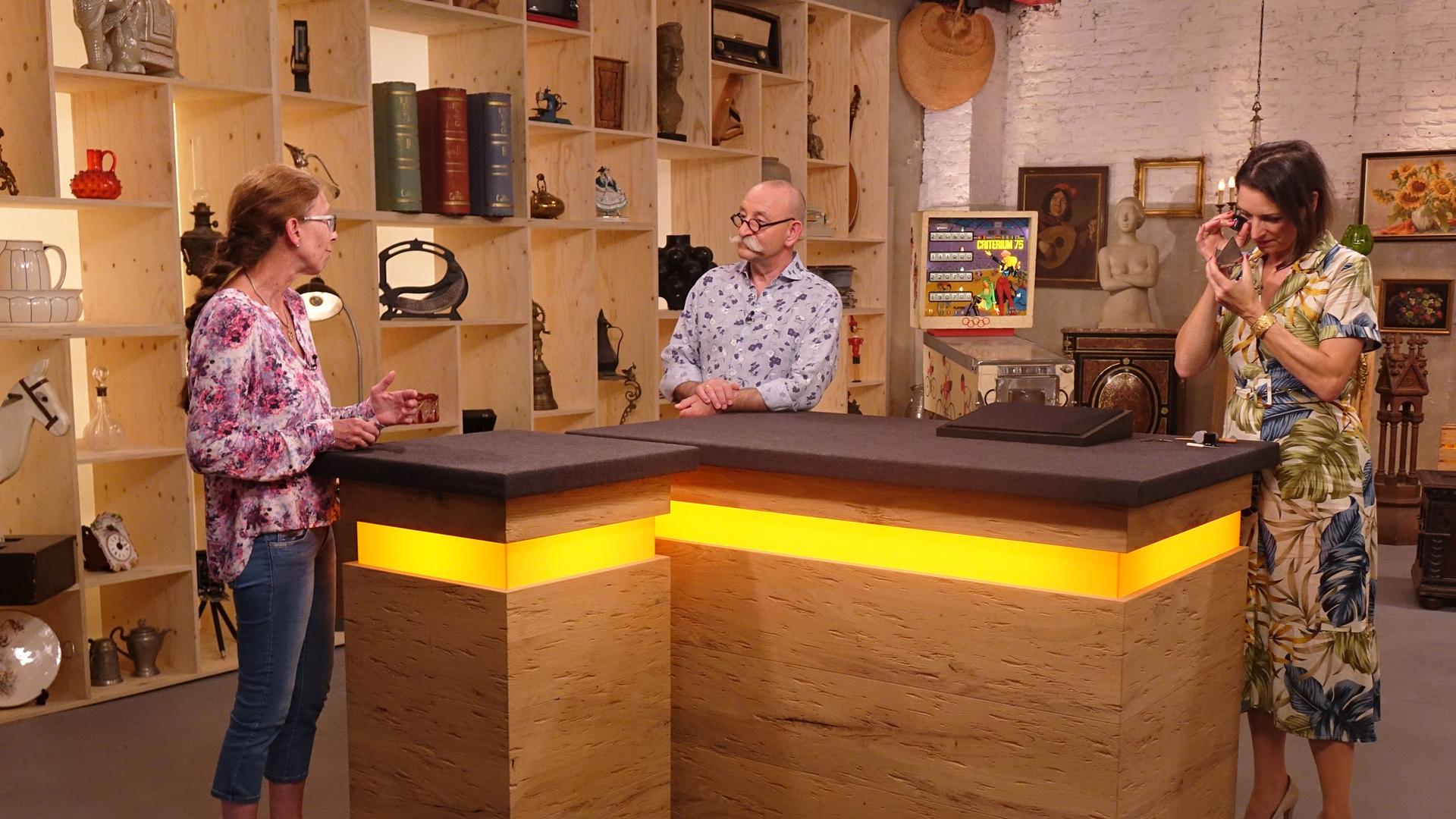 Expertin Wendela Horz (rechts) betrachtet ein Schmuckstück mit einem Vergrößerungsglas. Horst Lichter (Mitte) spricht mit der Verkäuferin (links).