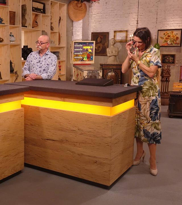 Expertin Wendela Horz (rechts) betrachtet ein Schmuckstück mit einem Vergrößerungsglas. Horst Lichter (Mitte) spricht mit der Verkäuferin (links).