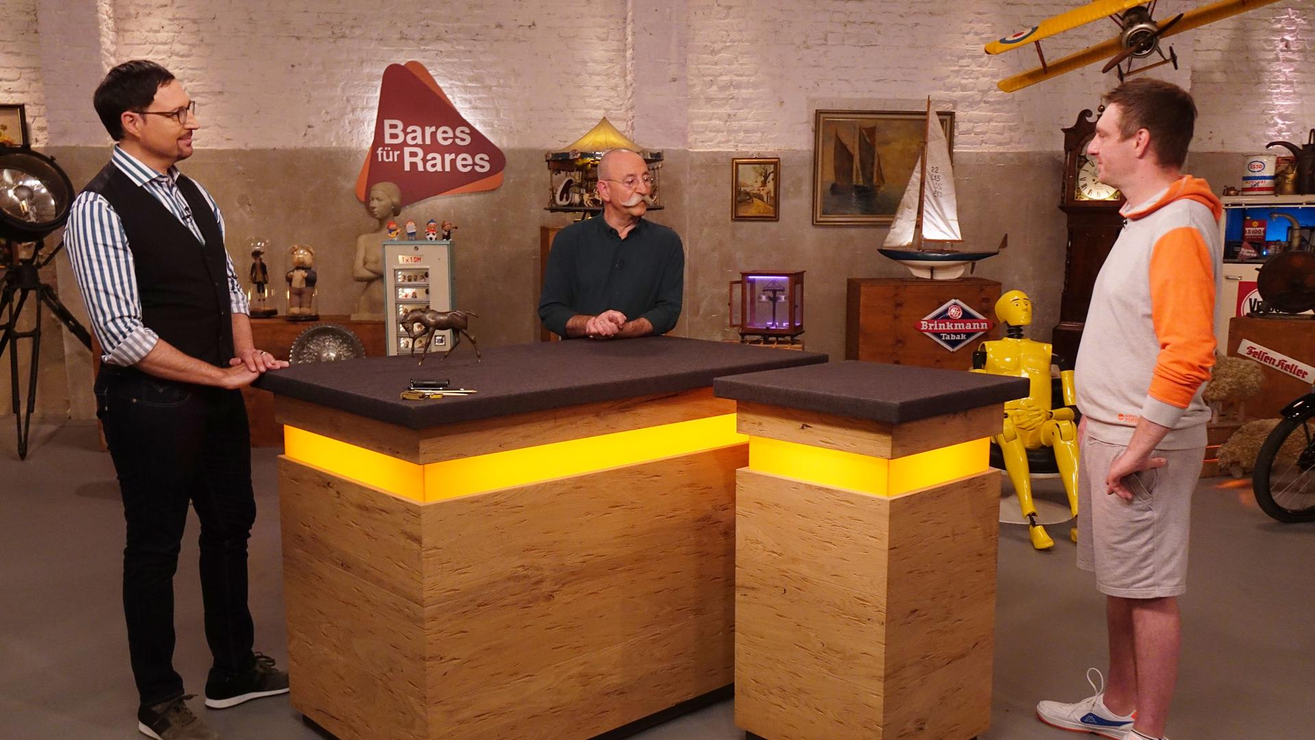 Experte Colmar Schulte-Goltz (links) hat eine Bronzefigur eines Pferdes vor sich auf dem Tisch stehen. Er und Horst Lichter (Mitte) schauen den Verkäufer (rechts) an.