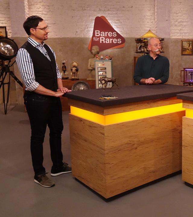 Experte Colmar Schulte-Goltz (links) hat eine Bronzefigur eines Pferdes vor sich auf dem Tisch stehen. Er und Horst Lichter (Mitte) schauen den Verkäufer (rechts) an.