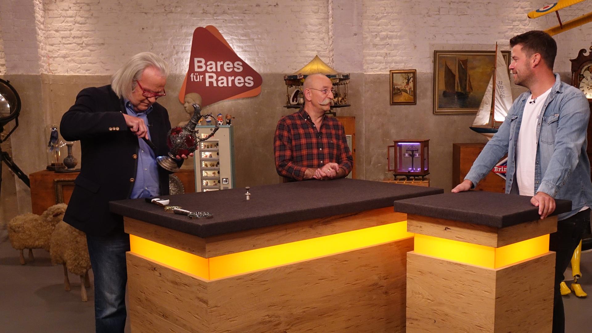 Experte Albert Maier (links) untersucht eine Kanne. Horst Lichter (Mitte) schaut den Verkäufer (rechts) an.