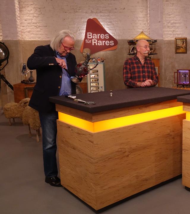 Experte Albert Maier (links) untersucht eine Kanne. Horst Lichter (Mitte) schaut den Verkäufer (rechts) an.