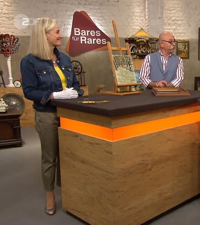 Expertin Dr. Friederike Werner steht links neben einem kleinen Gemälde, das auf einer kleinen Staffellei drapierten auf dem Expertisentisch steht. Sie und Horst Lichter (Mitte) schauen den Verkäufer (rechts) an.