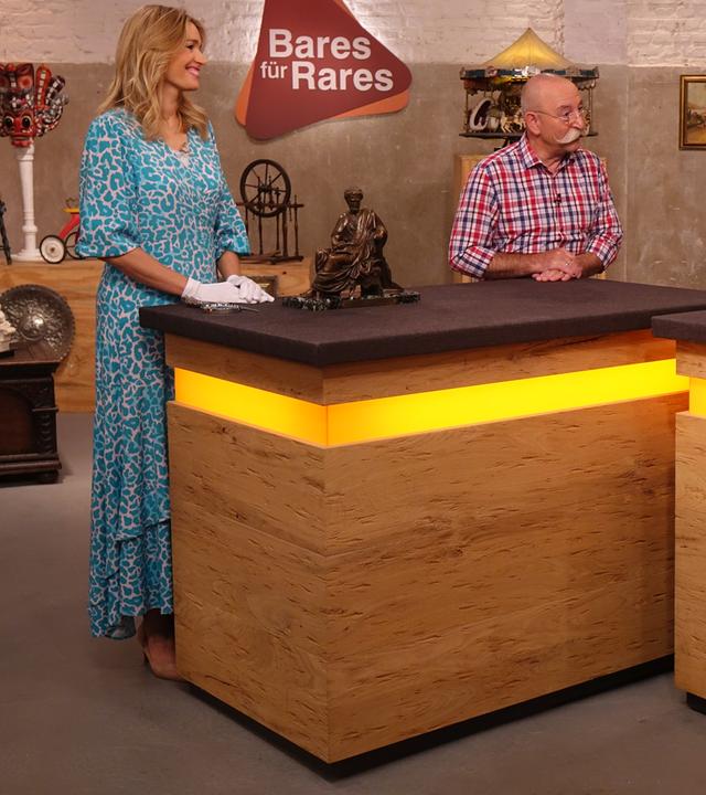 Expertise von Dr. Bianca Berding (links) zu einer Bronzeskulptur, die eine sitzende Person zeigt und neben ihr auf dem Tisch steht. Sie und Horst Lichter (Mitte) sehen den Verkäufer (rechts) an.