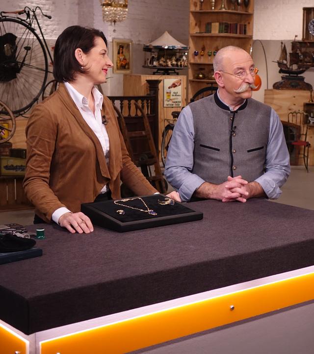 Expertin Wendela Horz (links) hat ein Schmuckset vor sich auf dem Tisch stehen. Sie und Horst Lichter (Mitte) schaut den Verkäufer (rechts) an.