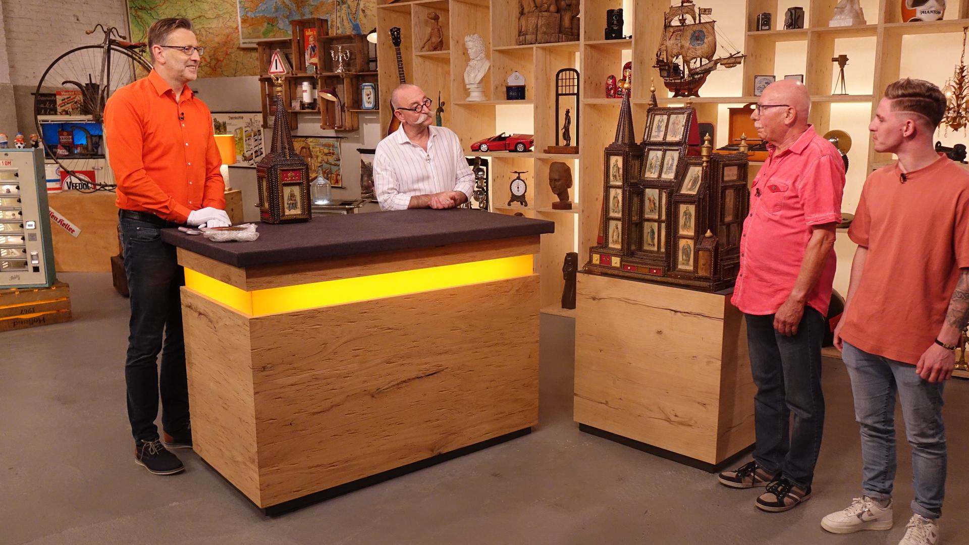 Experte Detlev Kümmel und Horst Lichter (links) sprechen mit den beiden Verkäufern (rechts) über eine in der Mitte aufgebaute Spieluhr in Form eines Doms aus dunklem Holz.