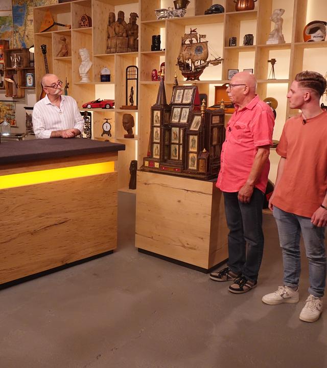 Experte Detlev Kümmel und Horst Lichter (links) sprechen mit den beiden Verkäufern (rechts) über eine in der Mitte aufgebaute Spieluhr in Form eines Doms aus dunklem Holz.