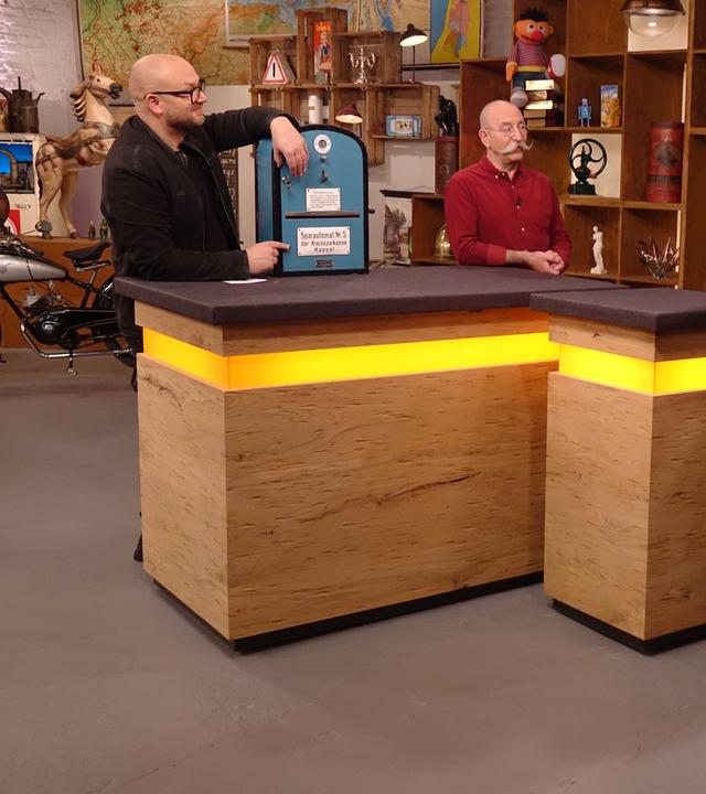 Experte Sven Deutschmanek (links) hat einen Automaten vor sich auf dem Tisch stehen. Er und Horst Lichter (Mitte) schauen die Verkäufer (rechts) an.