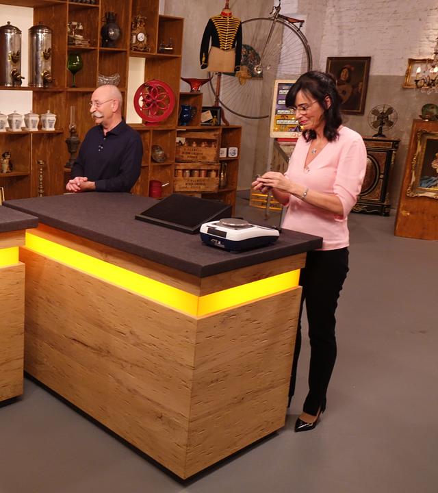 Expertin Dr. Heide Rezepa-Zabel (rechts) überprüft ein Schmuckstück an einer Waage, während Horst Lichter (Mitte) mit der Verkäuferin (links) spricht.