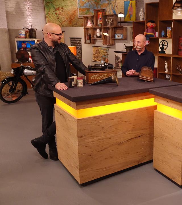 Experte Sven Deutschmanek (links) hat einen Phonographen vor sich auf dem Tisch stehen. Er spricht mit Horst Lichter (Mitte) und den beiden Verkäufern (rechts).