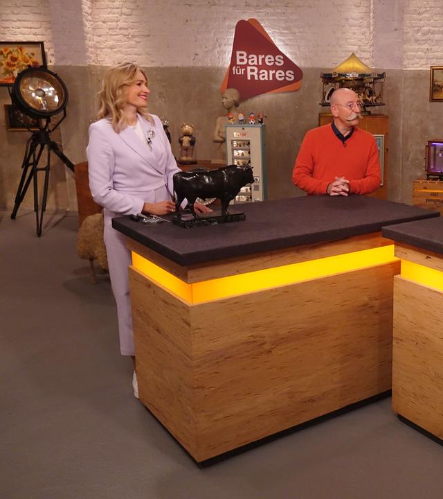 Expertin Dr. Bianca Berding (links) hat einen Bronze-Stier vor sich auf dem Tisch stehen. Sie und Horst Lichter (Mitte) schauen den Verkäufer (rechts) an.