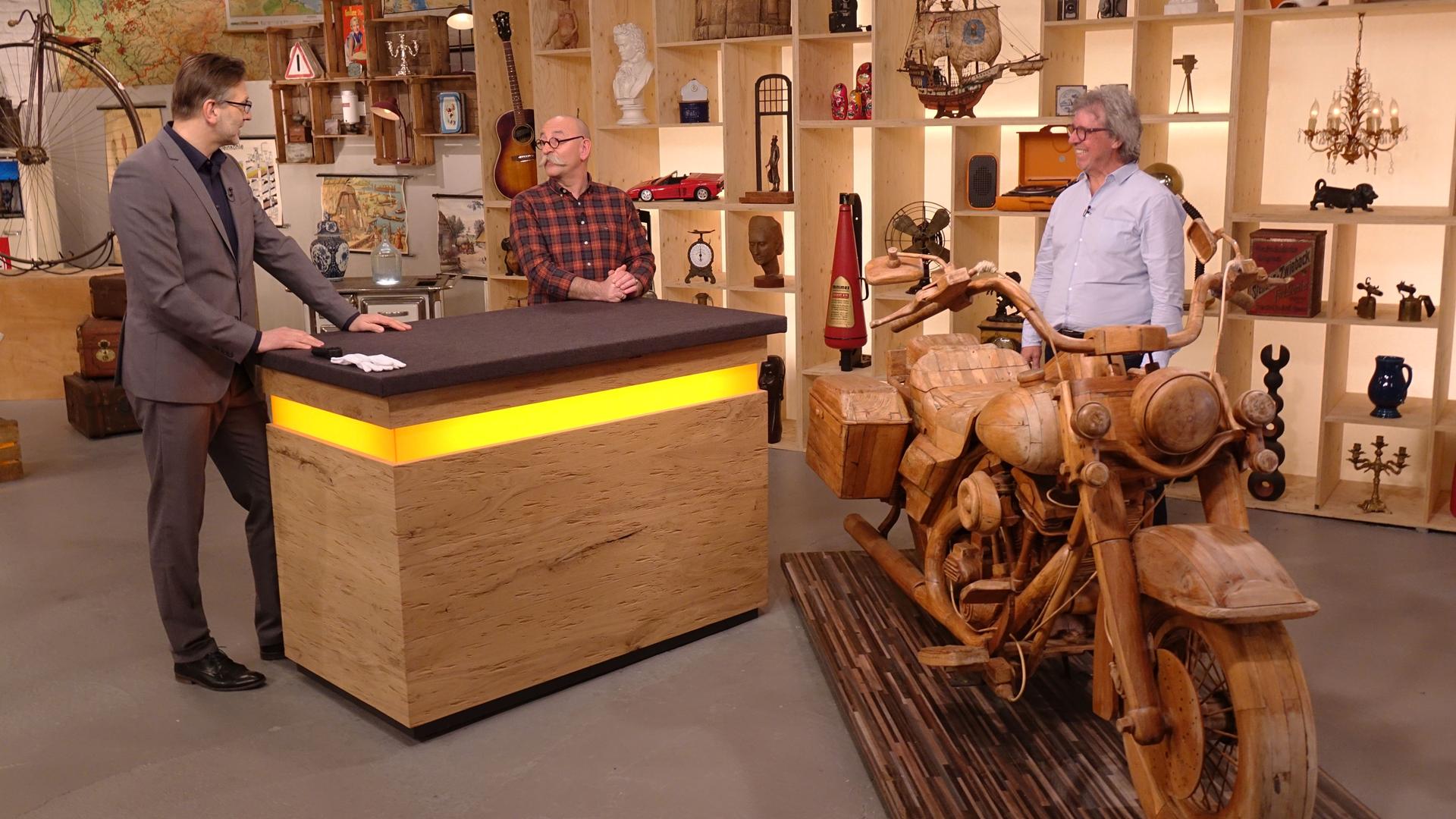 Experte Detlev Kümmel begutachtet ein Motorrad aus Holz. Neben ihm stehen Horst Lichter und der Verkäufer des Objekts.
