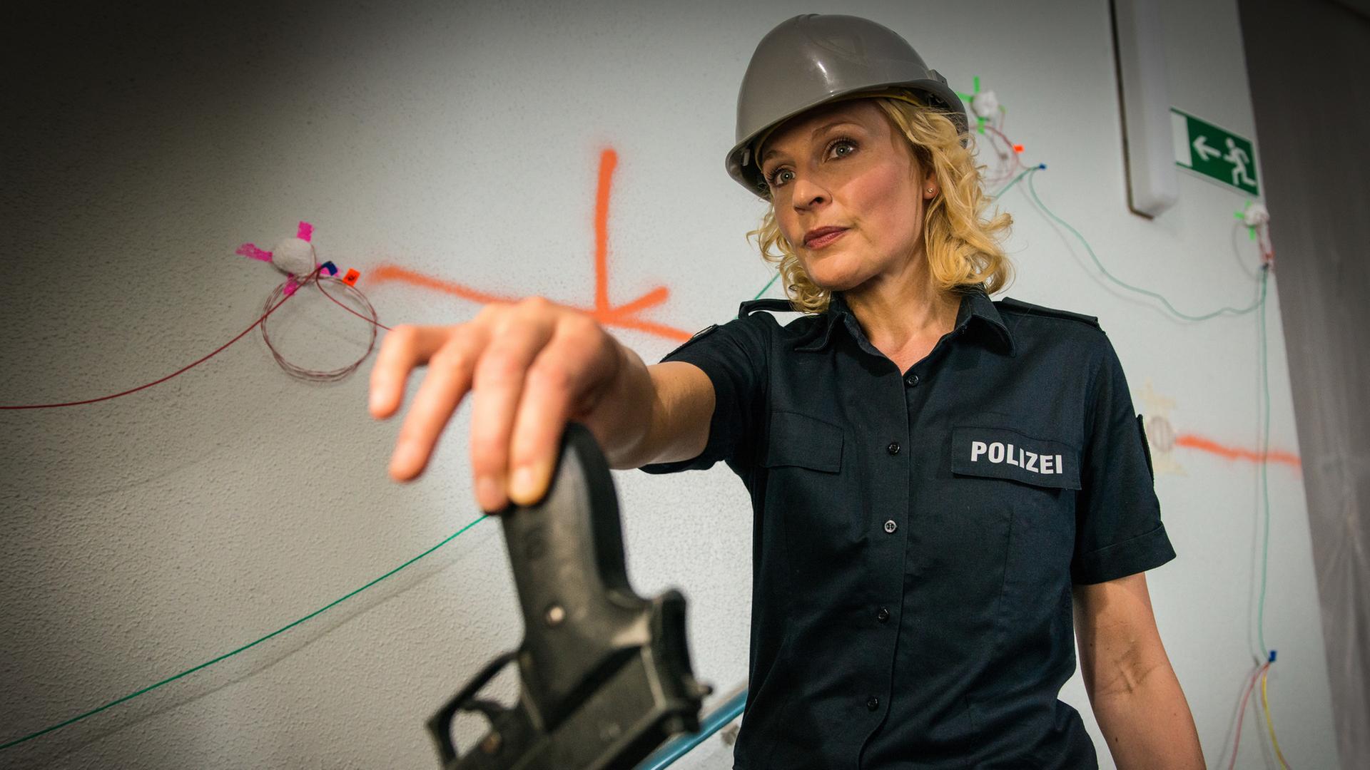 "Notruf Hafenkante - Explosive Lage": Die Polizeibeamtin Melanie Hansen (Sanna Englund) hält jemandem mit ausgestrecktem Arm ihre Waffe hin. Sie trägt einen grauen Bauhelm.