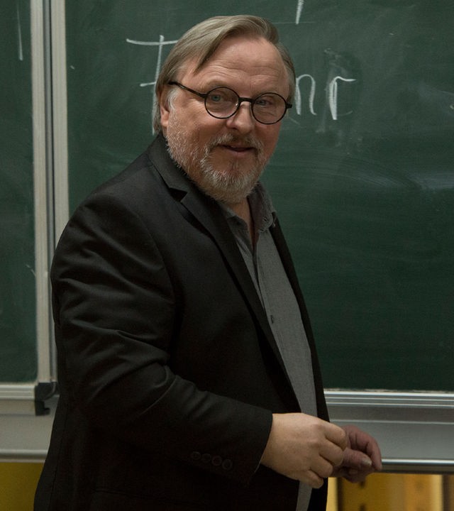 "Extraklasse": Ralph Friesner (Axel Prahl) steht seitlich zu einer Schultafel, sein Blick ist frontal gerichtet. Auf der Tafel ist sein Name geschrieben.