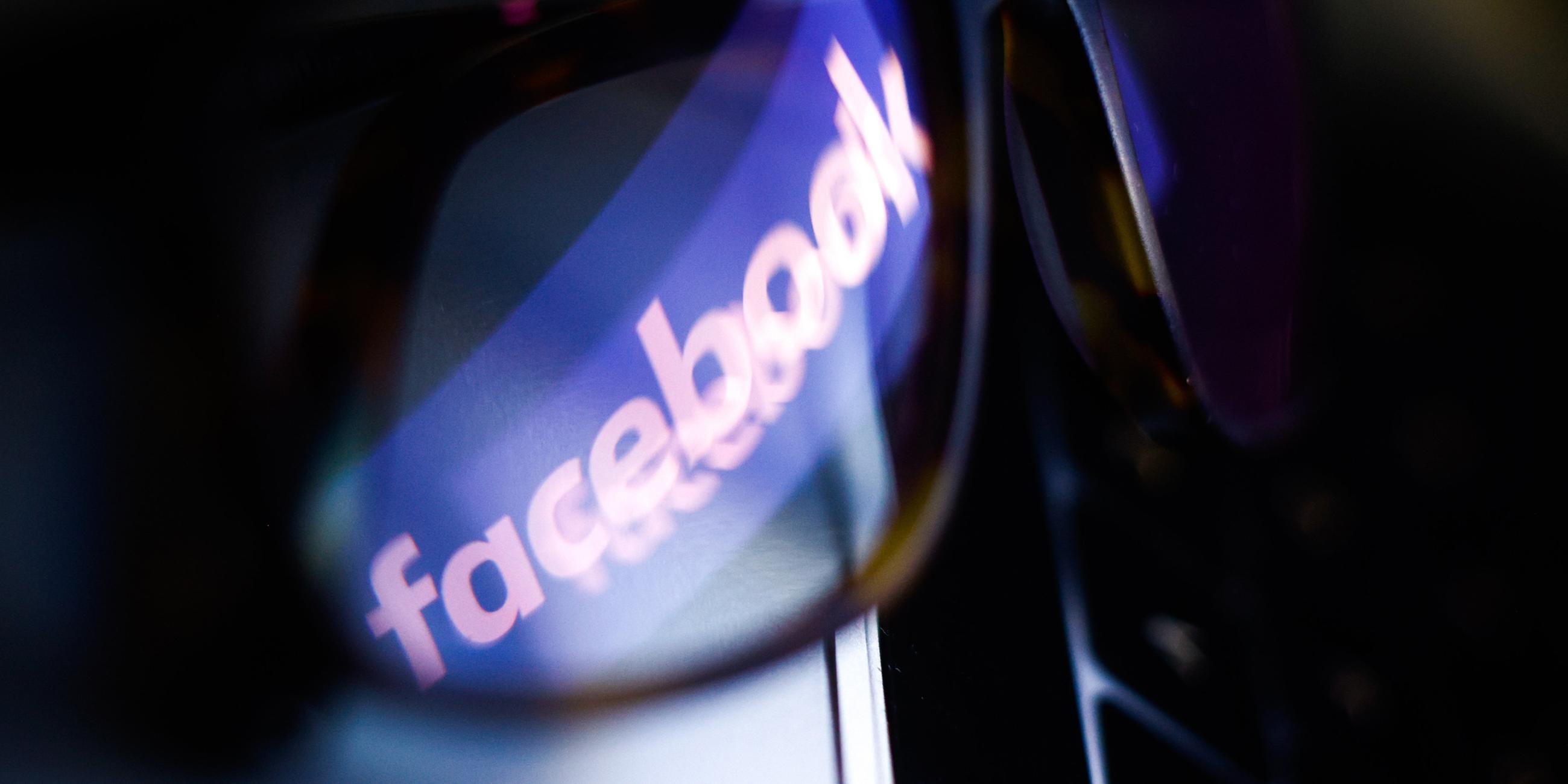 Das Logo von Facebook schimmert durch eine Brille auf einer Computer-Tastatur