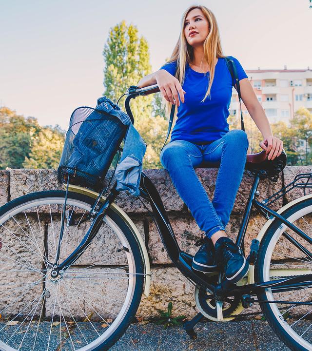 Frau sitzt auf einer Mauer, davor angelehnt steht ihr Fahrrad